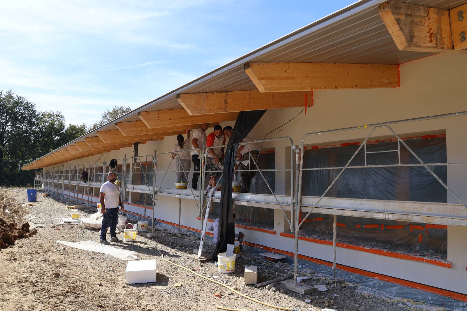 Façade du groupement scolaire Villemur-sur-Tarn en cours de construction, avec des ouvriers sur échafaudages réalisant les travaux, octobre 2025.